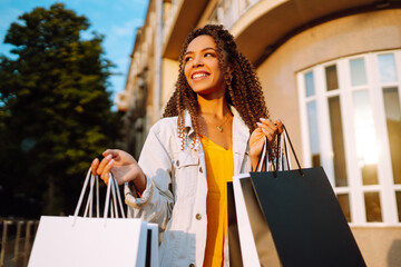 Young woman with shopping bags walking on street. Fashionable african american model carrying...
