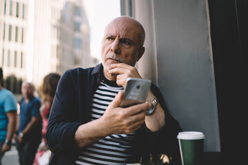 Thoughtful aged man using smartphone in street cafe