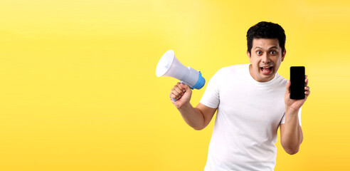 Shock and surprise face of Asian man holding megaphone and  presenting smart phone on yellow background in studio With copy space.