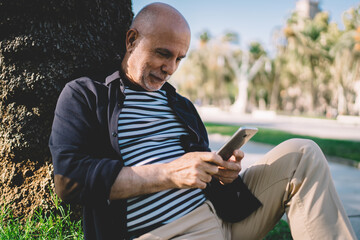 Fototapeta premium Smiling elderly man messaging on smartphone in park