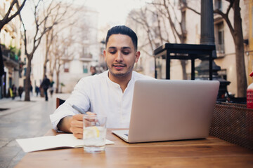 Serious young man in casual clothing working from sidewalk cafe