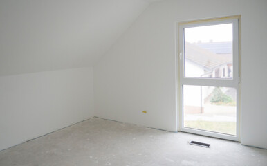White empty ready-to-paint room with attic ceiling and French window.Design of attic bedroom with slope of roof,panoramic window,attic space.Niche in floor for built-in heating convector.Copy space