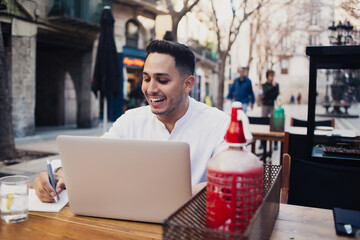 Smiling man sitting at sidewalk cafe and working on laptop