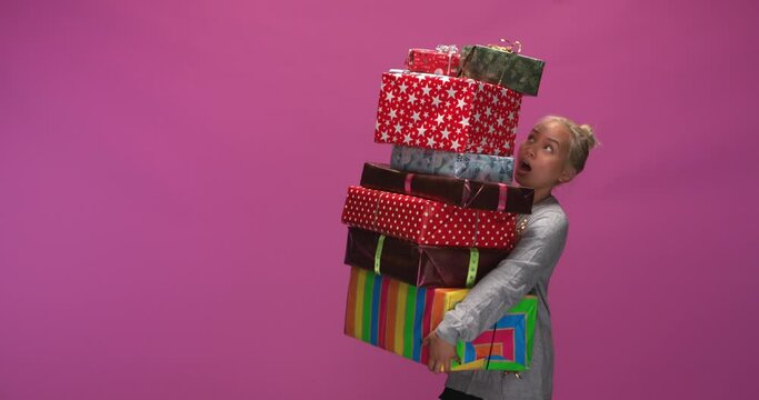 Studio, slow motion, young woman unsuccessfully tries to balance a stack of Christmas presents