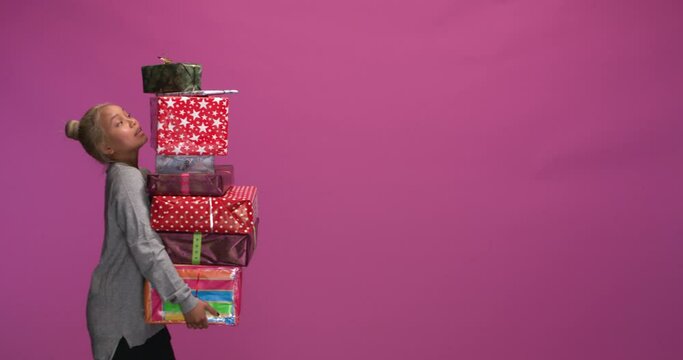 Studio, slow motion, young woman walks with a stack of Christmas presents