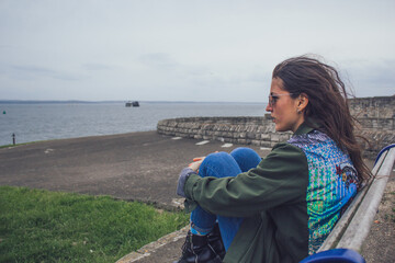 mujer sola nostálgica mirando hacia el mar desde paseo marítimo en invierno en día nublado