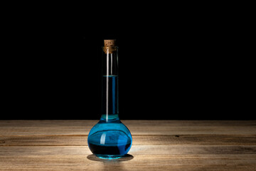Obraz na płótnie Canvas Still life of bottle of poison or perfume. Still life of glass bottle with blue liquid. Antique glass bottle on black background. Cork style bottle. Copy space for text.