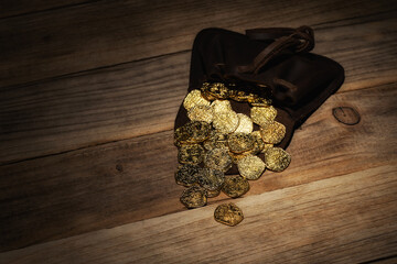 Leather pouch with poured gold coins on wooden background. Money, financial, growth concept.
