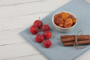 a bowl of apple jam, red apples and cinnamon sticks on blue napkin on white wooden background flat lay