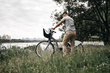 A guy with a bike on the river bank in a city park. City transport, walks in the city.