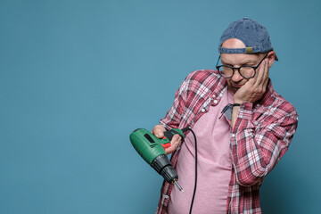 Upset Caucasian man looks at his broken electric drill and wonders what to do. Home repairs. Copy...