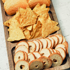 Mix of chips, snacks and crackers on a wooden stand. Unhealthy food, beer snack, ready meal. Close Up