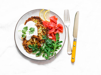 Zucchini and latkes with smoked salmon, sour cream and arugula. Delicious breakfast, brunch, tapas, appetizer on a light background, top view