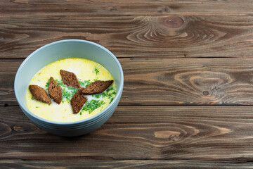 Cheese soup with croutons and dill on a wooden background.