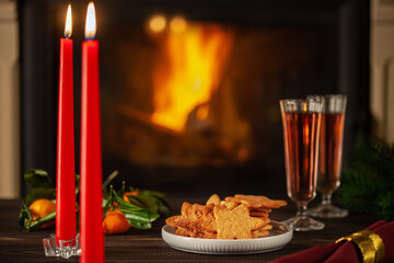 Homemade Christmas cookies on the table, glasses of wine and candles near the fireplace. Romantic New Year's Eve.