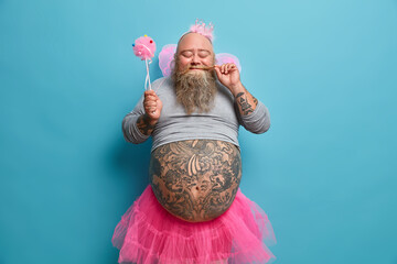 Positive funny bearded male princess holds magic wand and entertains guests on costume party shows...