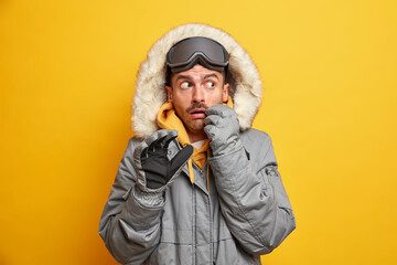 Winter adventure travel tourism concept. Scared European man in outerwear with fur hood rests in...
