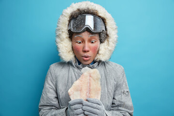 Shocked embarrassed Afro American woman stares at frozen fish feels comfortable in warm clothing...