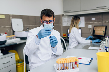 Two scientists or technicians with face protective masks work in laboratory on human blood samples.