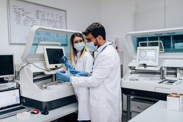 Fototapeta premium Two scientists or technicians with face protective masks work in laboratory on human blood samples.