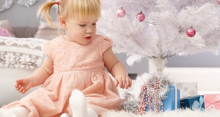 Fototapeta premium Little girl sitting under christmas tree, playing.