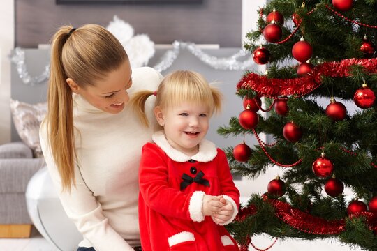 Young mother and happy little daughter sitting by christmas tree.