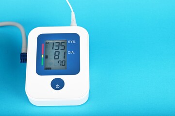 Digital blood pressure monitor on a blue background, close-up, shows high blood pressure