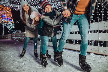 Happy young family having fun and enjoying in beautiful winter night at frozen skating park.