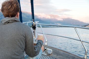 Man on yacht drinking morning coffee. Traveling on sailboat. Traveler meeting sunrise. Lifestyle authentic moment. Back view.