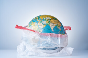 The concept of protecting the world from plastic waste, fighting environmental pollution, fighting for the environment, a globe in a white garbage bag on a light background.