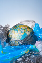 The concept of protecting the world from plastic waste, fighting environmental pollution, the globe lies in a pile of various garbage layouts on a light background.