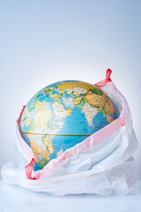 The concept of protecting the world from plastic waste, fighting environmental pollution, fighting for the environment, a globe in a white garbage bag on a light background.