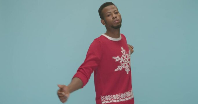 Studio, slow motion, young man in a Christmas sweater dances against a blue background