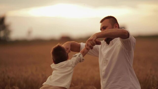 Stock video of a cheerful dad spinning his boy holding hands on a meadow. Jolly father and his little son having fun together at sunset. Happy Father s day.