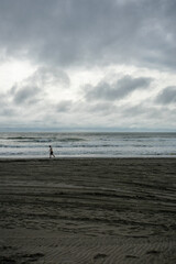 Fototapeta na wymiar A Lonely Man Walking Across the Beach With A Dramatic Stormy Sky Behind Him
