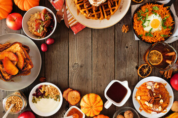 Assorted autumn breakfast or brunch items. Frame against a dark wood background. Pumpkin spice pancakes, waffles, apple french toast, oatmeal, egg skillet, yogurt. Overhead view. Copy space.