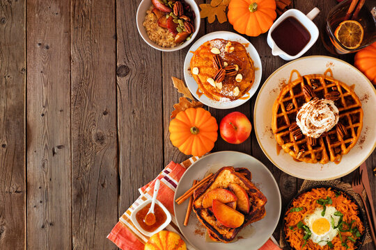 Assorted autumn breakfast or brunch items. Side border against a dark wood background. Pumpkin spice pancakes, waffles, apple french toast, oatmeal, egg skillet. Overhead view. Copy space.
