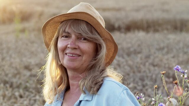 Smiling Middle Aged Woman Stands On The Field And Looks At The Camera. Romantic Image Of Beautiful Blonde In Hat.
