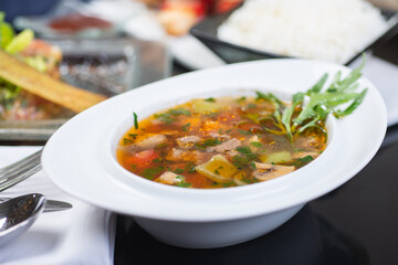 Traditional vegetable soup broth in a white plate on a table in a restaurant.