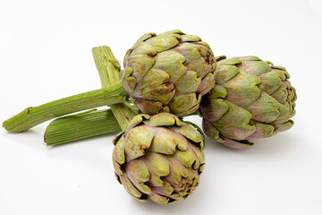 Obraz premium Three organic artichokes with a piece of stem on a white surface.