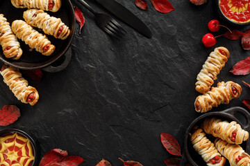 Halloween party food, mummy dogs and ketchup-mustard sauces on a black background with copy space