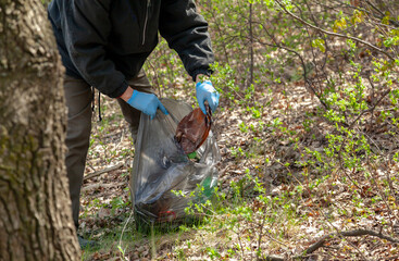 Fototapeta premium Man in gloves collects plastic trash in forest