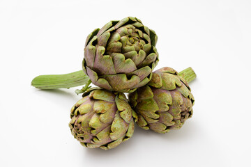 Three organic artichokes with a piece of stem on a white surface.
