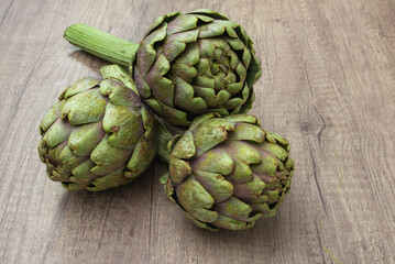 Fototapeta premium Three fresh organic purple artichokes with stem on a rustic wooden surface and dark background
