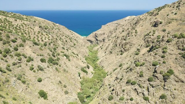 Aerial view of a narrow gorge heading towards a clear, blue ocean (Richtis Gorge, Crete, Greece)