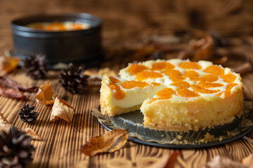 Cheesecake oder Käsekuchen mit fruchtigen orangen Mandarinen auf einem Tisch aus Holz im Herbst mit Laubblättern