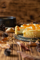 Cheesecake oder Käsekuchen mit fruchtigen orangen Mandarinen auf einem Tisch aus Holz im Herbst mit Laubblättern