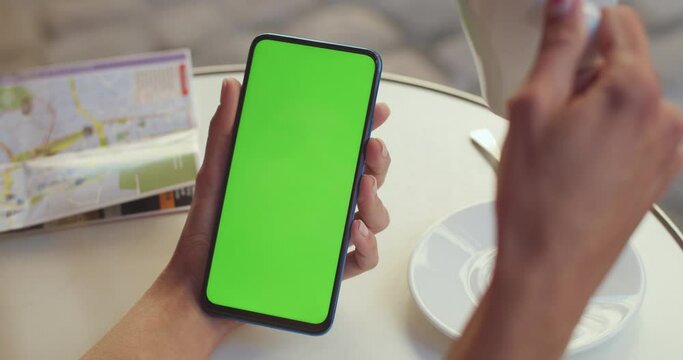 Close up view of female hands with trendy fingernails design holding smartphone with mockup screen and drinking coffee. Concept of greenscreen and chroma key.