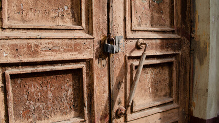 The lock on the old wooden door closeup. Rust on the metal lock. Peeling brown paint on the old door. Ancient texture.