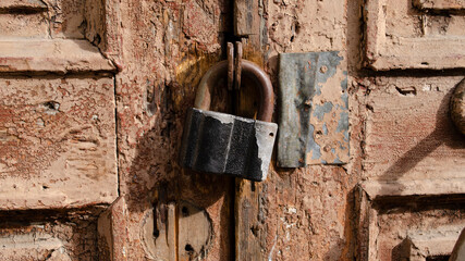 The lock on the old wooden door closeup. Rust on the metal lock. Peeling brown paint on the old door. Ancient texture.